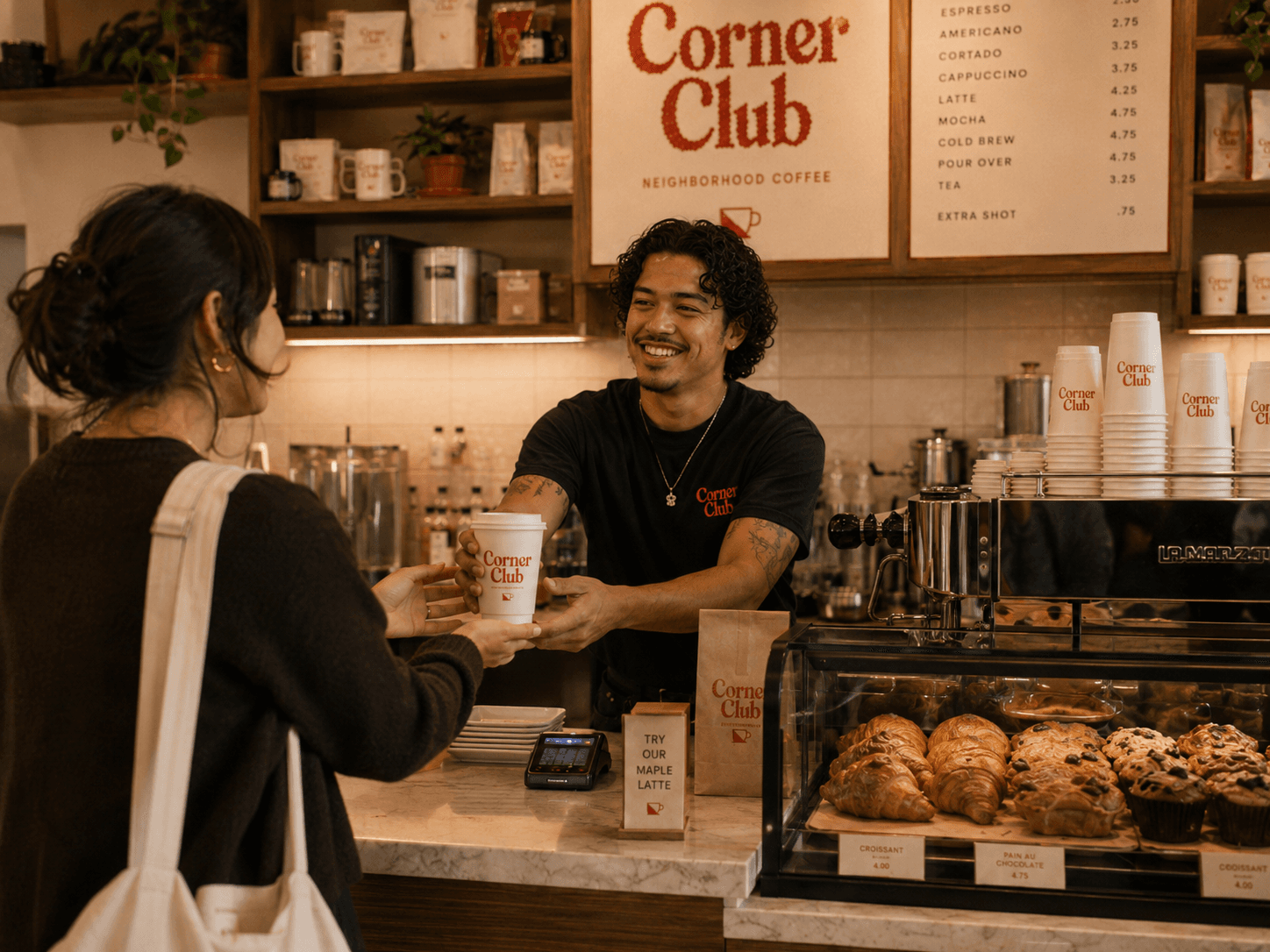 A Corner Club barista handing a takeaway cup across the marble counter, menu board above